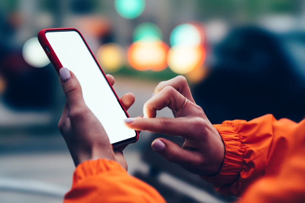 Close up view of female hands holding mobile phone touching mock up blank screen with finger. People using app on smartphone on street with bokeh blurred city lights. Texting message in social network